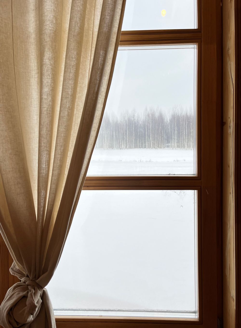 Snow-covered view through a rustic wooden window with curtains