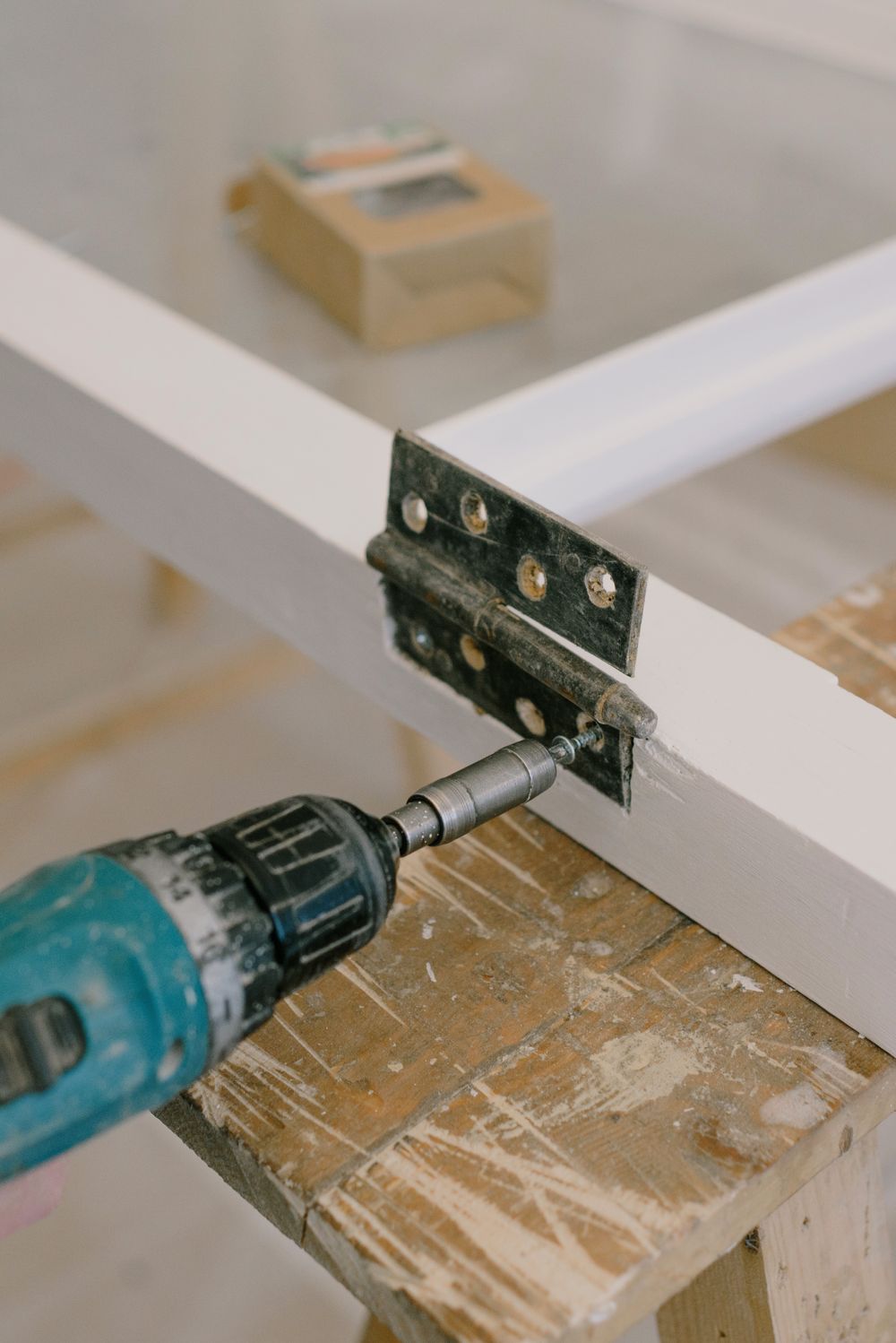 Electric screwdriver resting beside a hinge on a workbench
