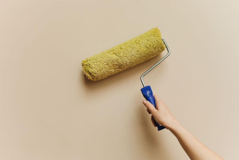 Hand rolling paint onto a wall with a yellow roller